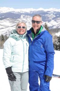 Two people dressed in ski gear in front of a snowy mountain scene.